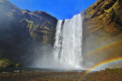 Scenic view of waterfall and rainbow against sky