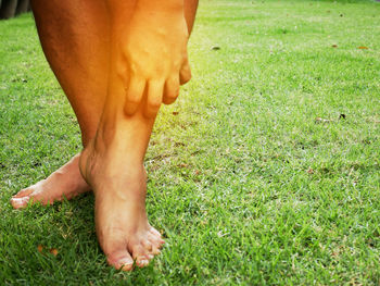 Low section of person scratching leg while standing on grassy field