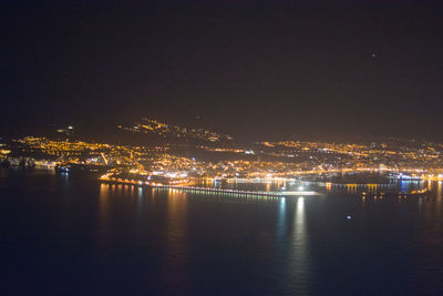 Illuminated city by sea against sky at night