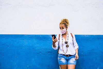 Young woman using mobile phone against wall