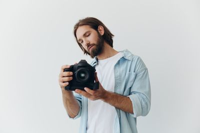 Young woman holding camera against white background