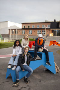 Portrait of teenage friends sitting in front of school