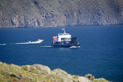 Ship sailing on sea against mountain