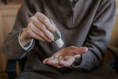 Midsection of senior man using hand sanitizer at home