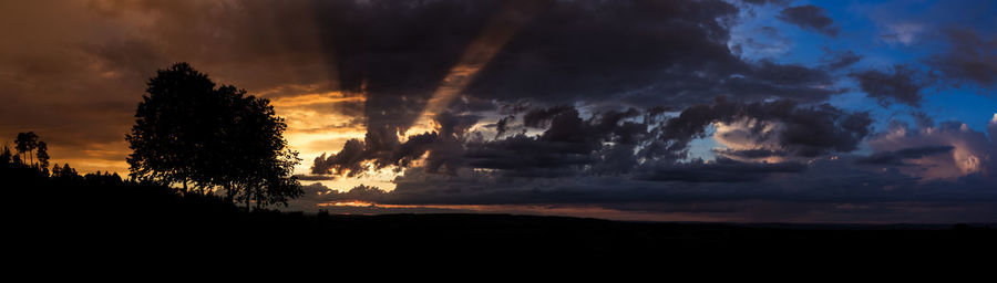 Silhouette trees against dramatic sky during sunset