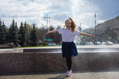 Happy little cute girl having fun in splashes a fountain