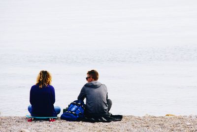 Rear view of friends sitting on shore at beach