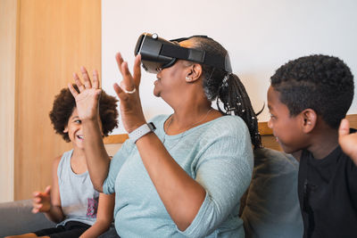 Grandmother using virtual reality goggles while sitting on sofa with kids at home