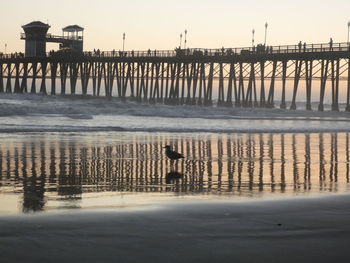 Pier on beach against sky during sunset