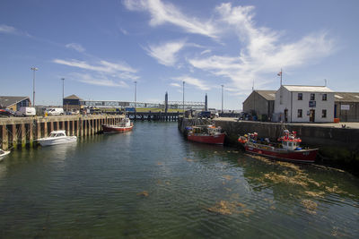 Sailboats moored in harbor by buildings against sky