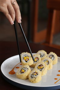 Close-up of woman hand holding sushi in plate on table