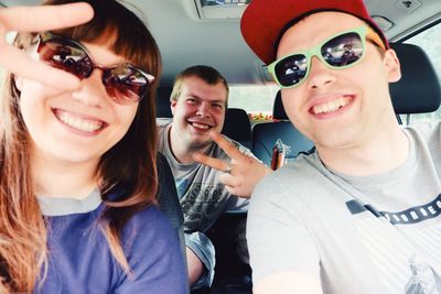 Portrait of happy friends showing peace sign in car