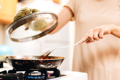 Young millennial woman at home in the kitchen cooking  on gas stove or range 