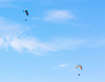 Low angle view of people paragliding against sky