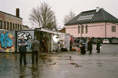 People on wet street against buildings in city