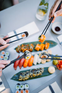 Vertical view of the friends hands holding sushi and rolls with wooden chopsticks