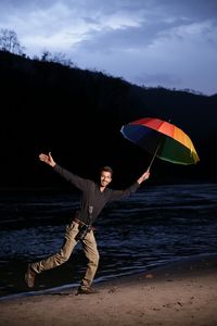 Portrait of man holding colorful umbrella by ganges river at dusk