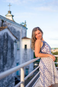 Portrait of young woman standing by railing