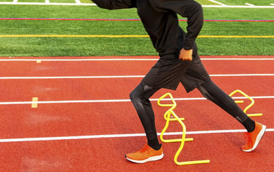 Low section of man running over hurdles at sport track