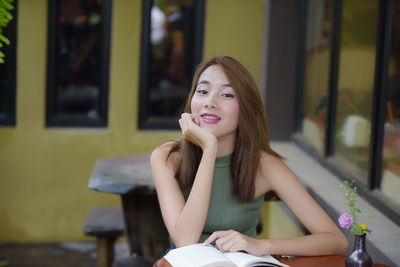 Portrait of young woman with book at table in cafe