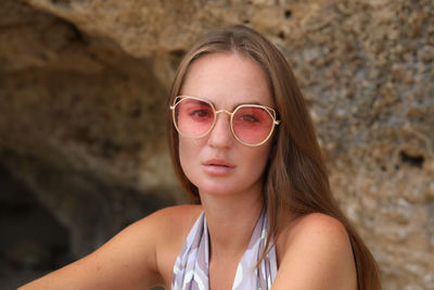 Portrait of woman wearing sunglasses sitting against rock