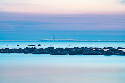 Bridge over sea against cloudy sky during sunset