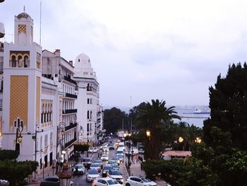 Cars on road by buildings in city against sky