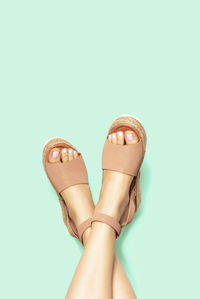 Female legs with a white pedicure in summer brown sandals on background, copy space