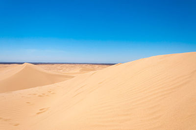 Sand dunes in desert against clear blue sky