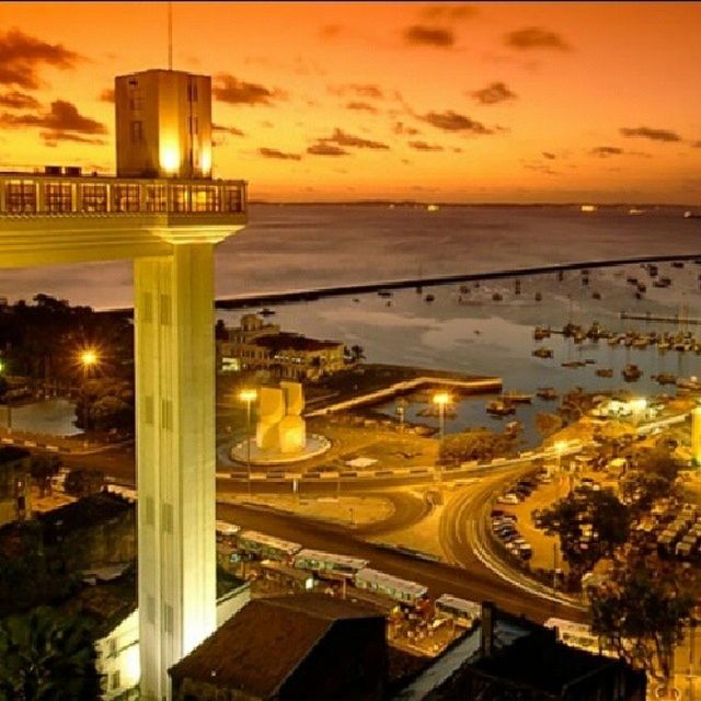 sunset, architecture, built structure, sea, illuminated, building exterior, water, orange color, sky, city, cloud - sky, horizon over water, dusk, high angle view, outdoors, cityscape, lighting equipment, no people, nature, scenics