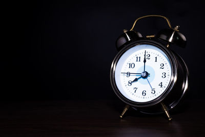 Close-up of clock on table against black background