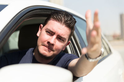 Frustrated man gesturing through window while traveling in car