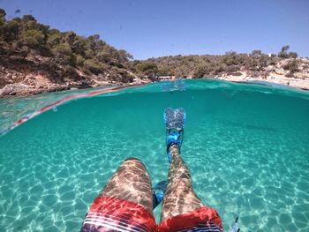 Low section of man swimming in sea against sky