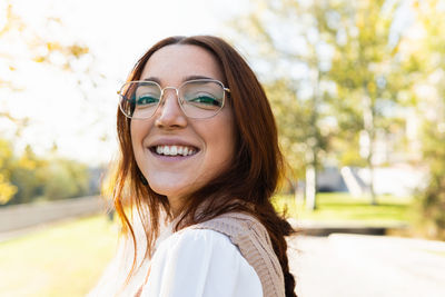 Close-up portrait of beautiful young woman with glasses smiling looking at camera in the park