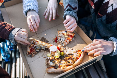 Four friends eating pizza outdoors, partial view