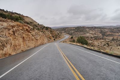 Empty road leading towards mountains against cloudy sky