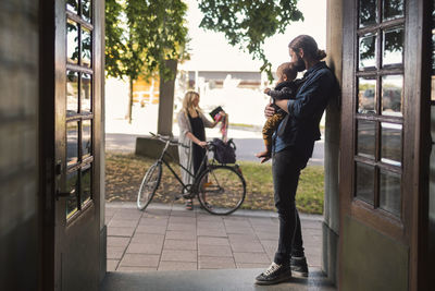 Father at door holding baby while looking at woman leaving for work