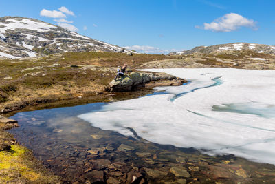 Full length of woman sitting by frozen lake against sky