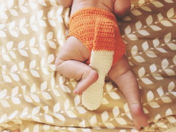 Low section of baby in knitted cloth relaxing on bed at home