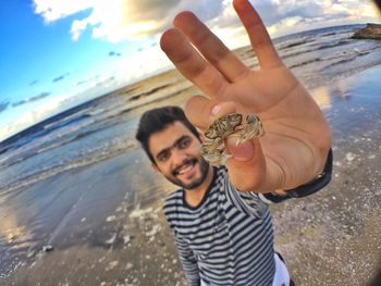 Portrait of young man showing crab while standing at beach