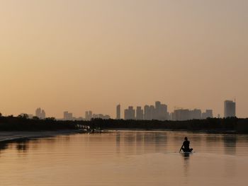 Silhouette man in river against buildings during sunset