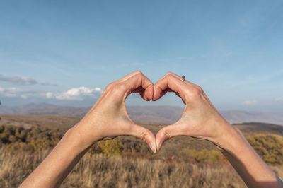 Midsection of man making heart shape against sky