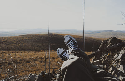 Low section of man sitting on cliff against landscape