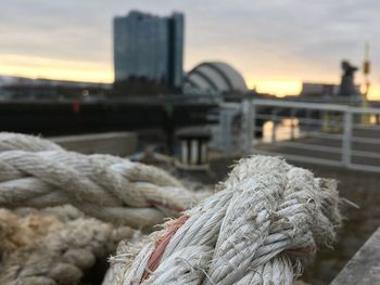 Close-up of rope tied to bridge at harbor against sky