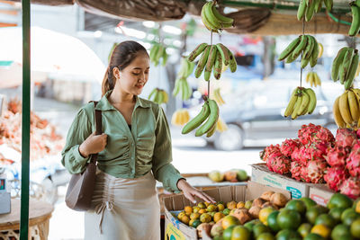 Portrait of young woman holding fruits at market stall