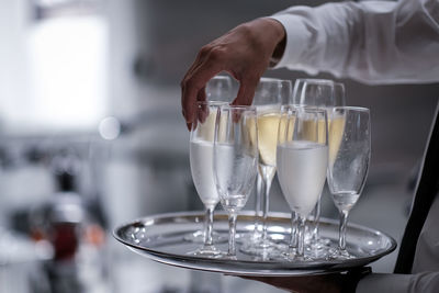 Cropped hands of person holding champagne flutes on tray