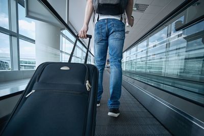 Man walking with suitcase. rear view of traveler on moving walkway at airport terminal.