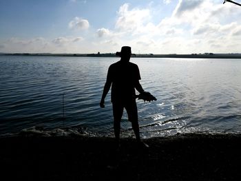 Silhouette man with fish standing by lake