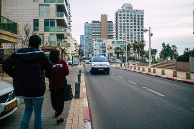 Rear view of people walking on road in city