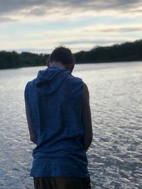 Rear view of man standing by lake during sunset